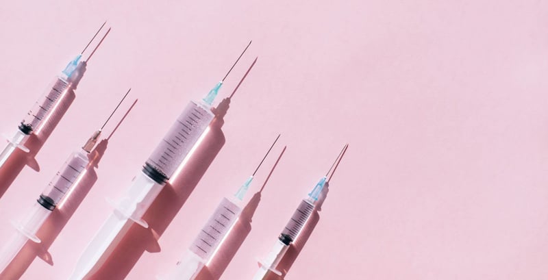 Image of several aesthetic treatment needles on a pink background