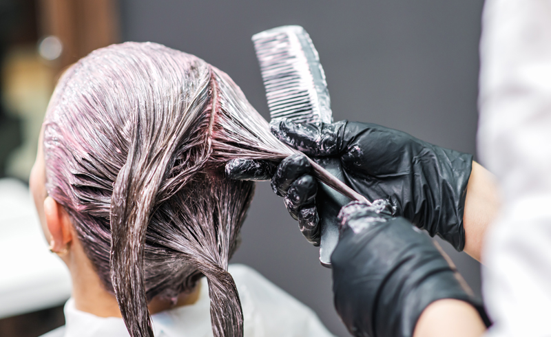 Close up image of a stylist applying colour to a woman's head of hair