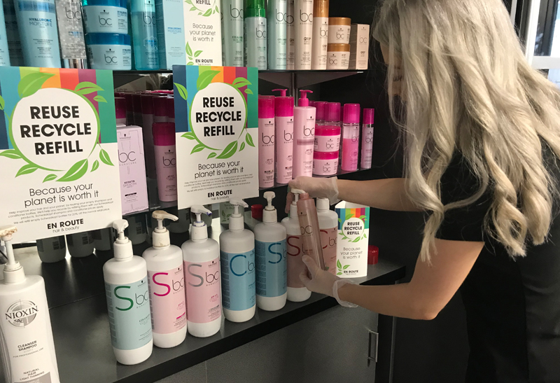 A woman stood at a hair salon retail display looking at a bottle of shampoo