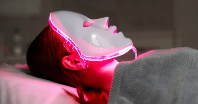 A woman laying down wearing an LED face mask