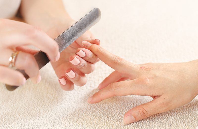 close up image of a nail technician filing a woman's nails