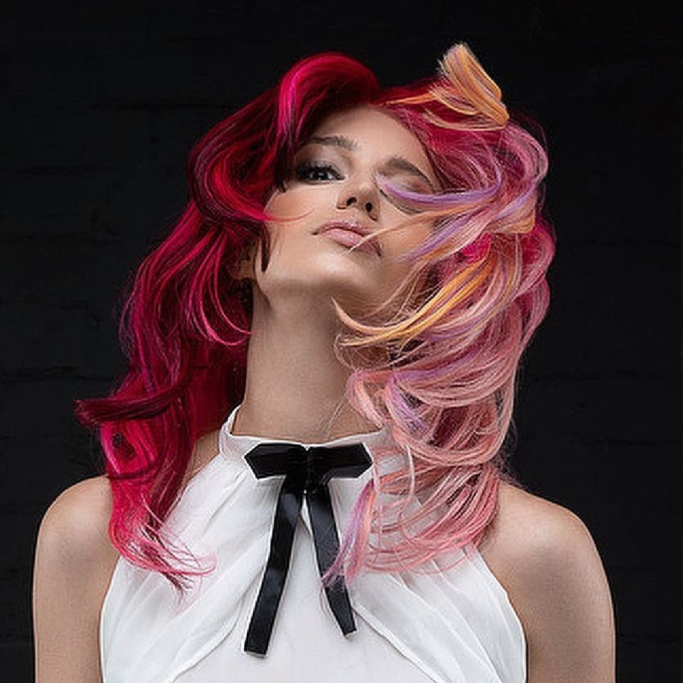 A model with red, pink and yellow coloured hair wearing a white top with a black bow