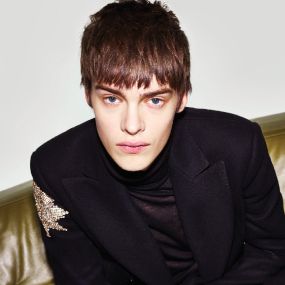 An image of a male model with short hair. Wearing and black jacket with a silver star on the shoulder