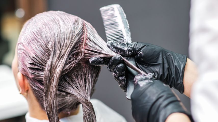Close up image of a stylist applying colour to a woman's head of hair