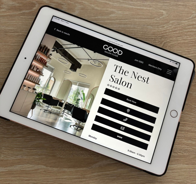 An iPad on a wooden table displaying The Nest Salon on Good Salon Guide's website