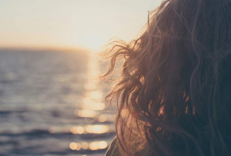 Woman with curly hair facing a sunset on a beach